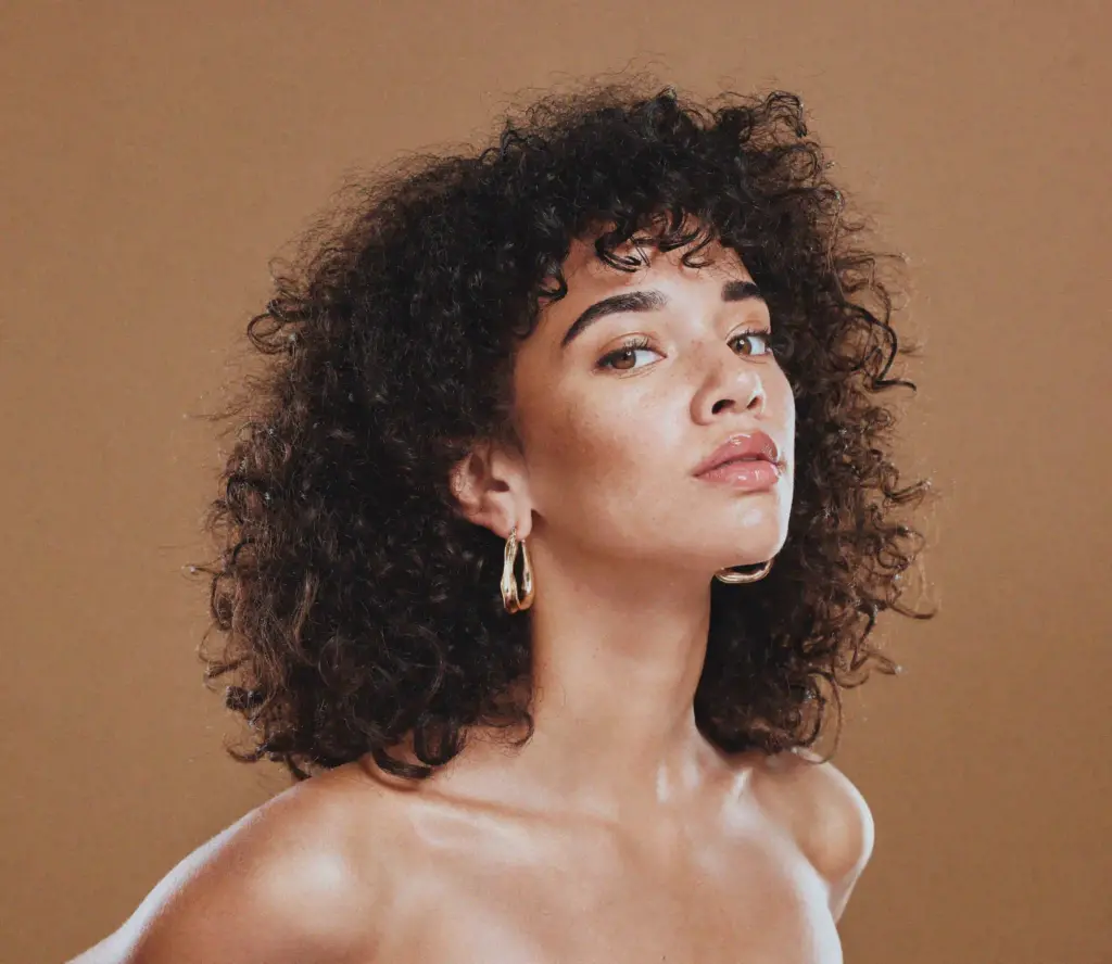 A woman with curly hair and large earrings, radiating elegance and style.