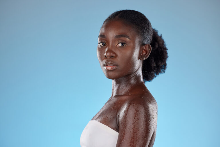 Confident woman with glowing, hydrated skin posing against a light blue background, symbolizing radiant beauty and advanced skincare.