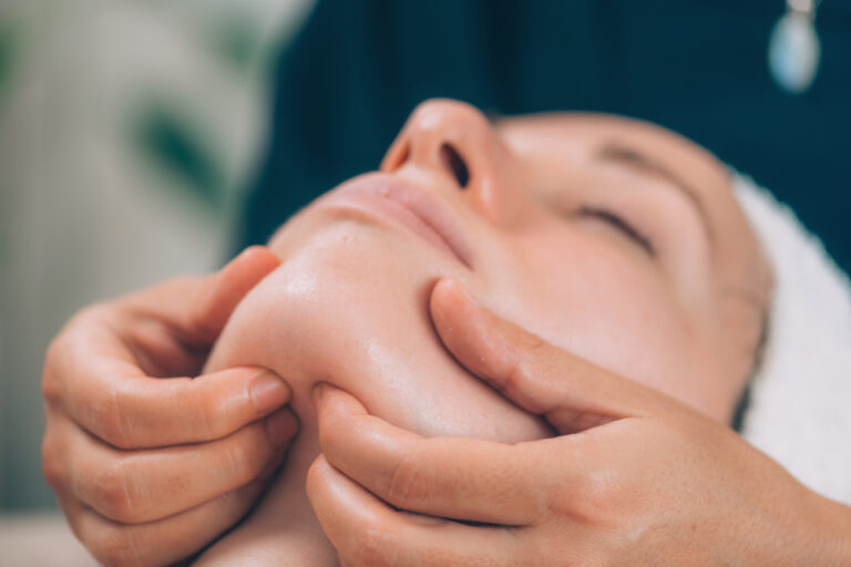 Woman receiving a gentle facial massage on a spa table, emphasizing a soothing treatment for sensitive skin.