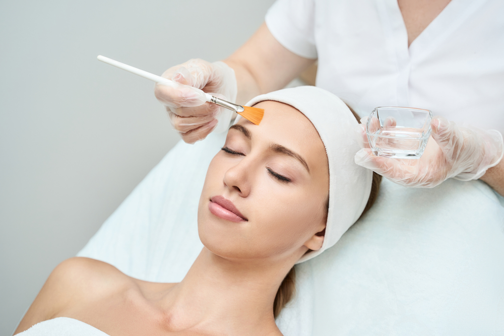 A serene woman receives a facial treatment with an applicator brush in a spa setting.