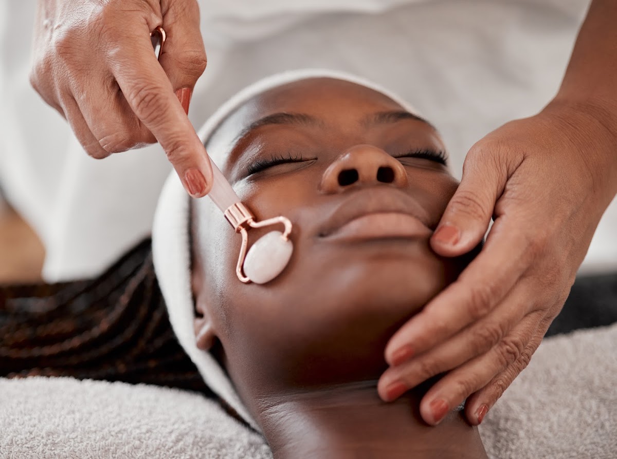 Woman enjoying a facial massage with a rose quartz roller at a spa.
