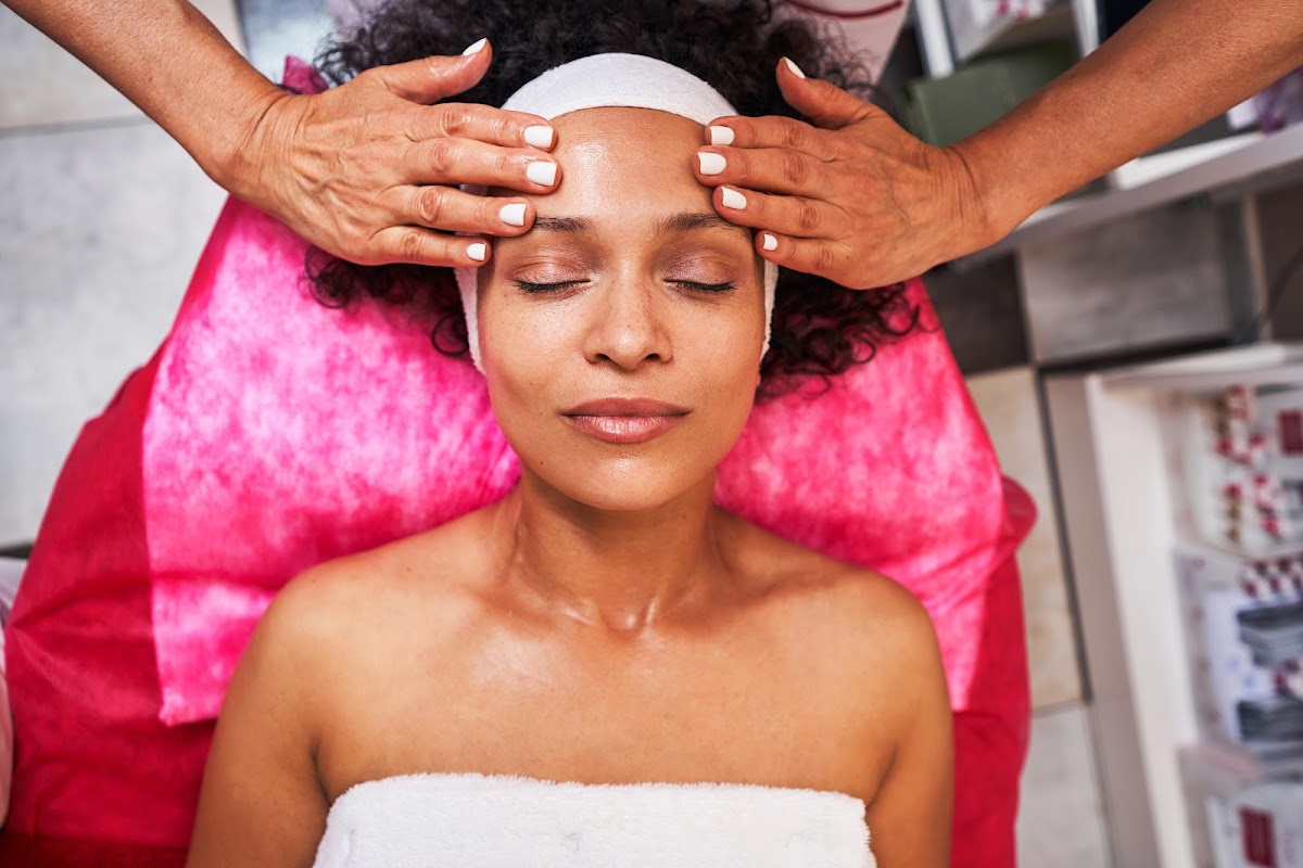 Woman enjoying a relaxing forehead massage at a spa, lying on a pink towel.