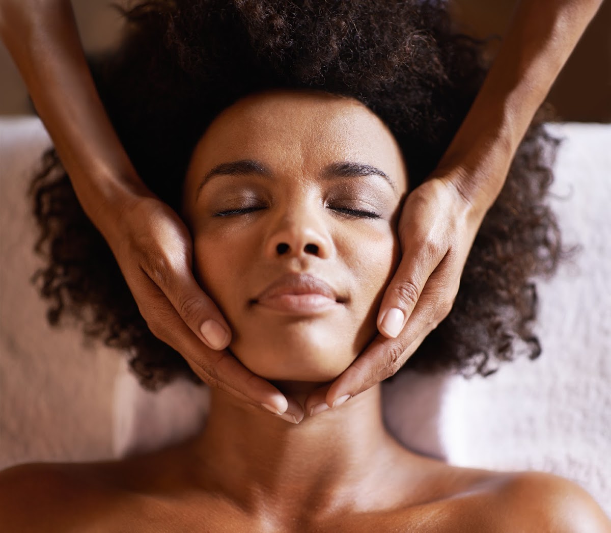 A woman with curly hair enjoys a soothing facial massage at a spa, her eyes closed in relaxation.