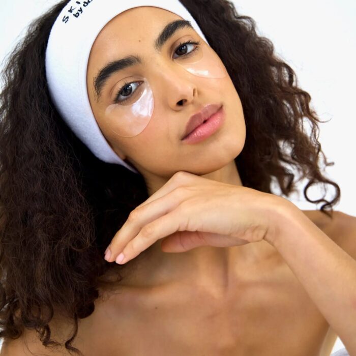 Woman with glowing skin wearing under-eye patches and a "Skin Studio by Doctor's Daughter" headband, highlighting a fresh and relaxed appearance