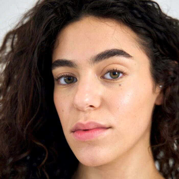 Portrait of a young woman with curly hair and glowing skin.