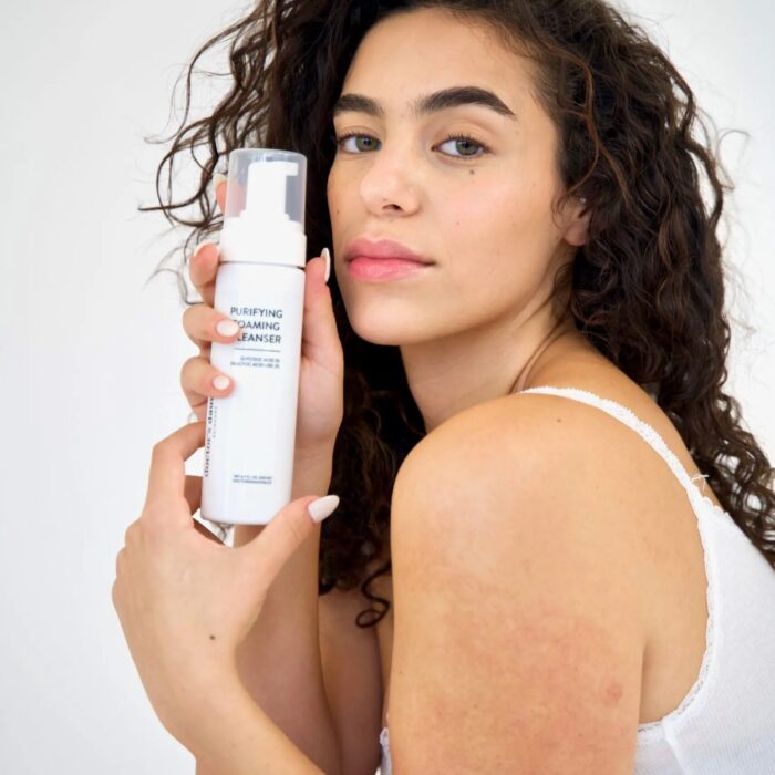 Woman holding skincare product with a confident expression