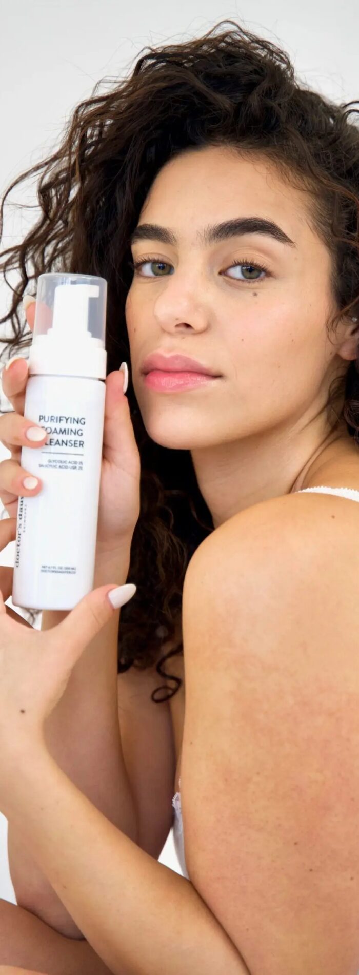 Woman holding skincare product with a confident expression
