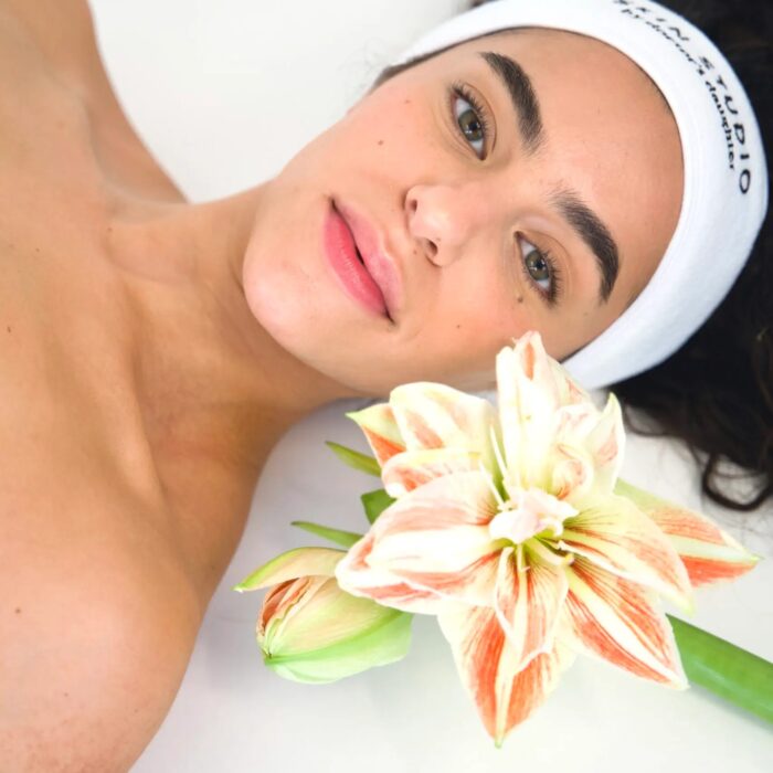 Woman with glowing skin wearing under-eye patches and a "Skin Studio by Doctor's Daughter" headband, highlighting a fresh and relaxed appearance